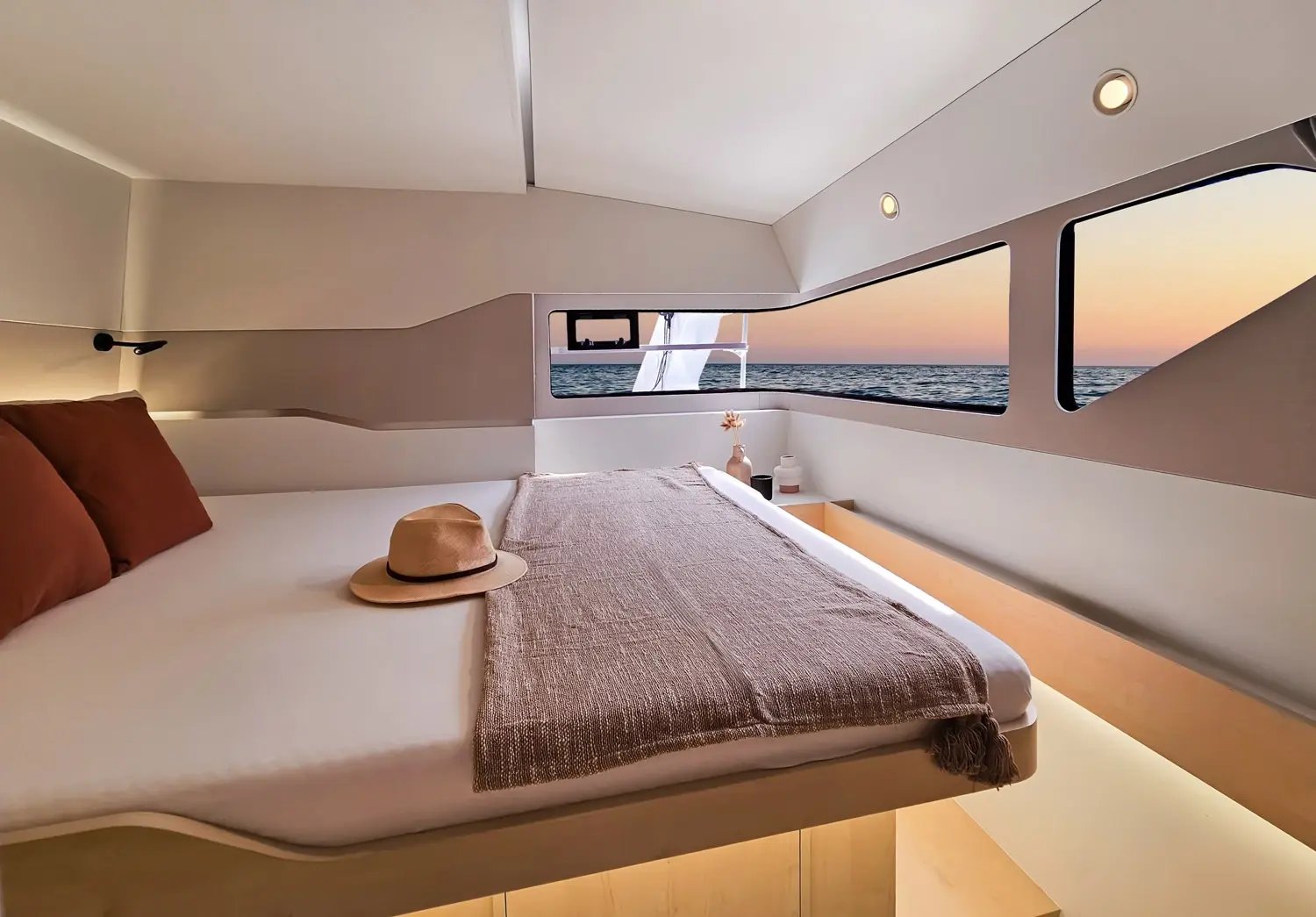 A cabin in a hull, with a double berth under a long window at sunset