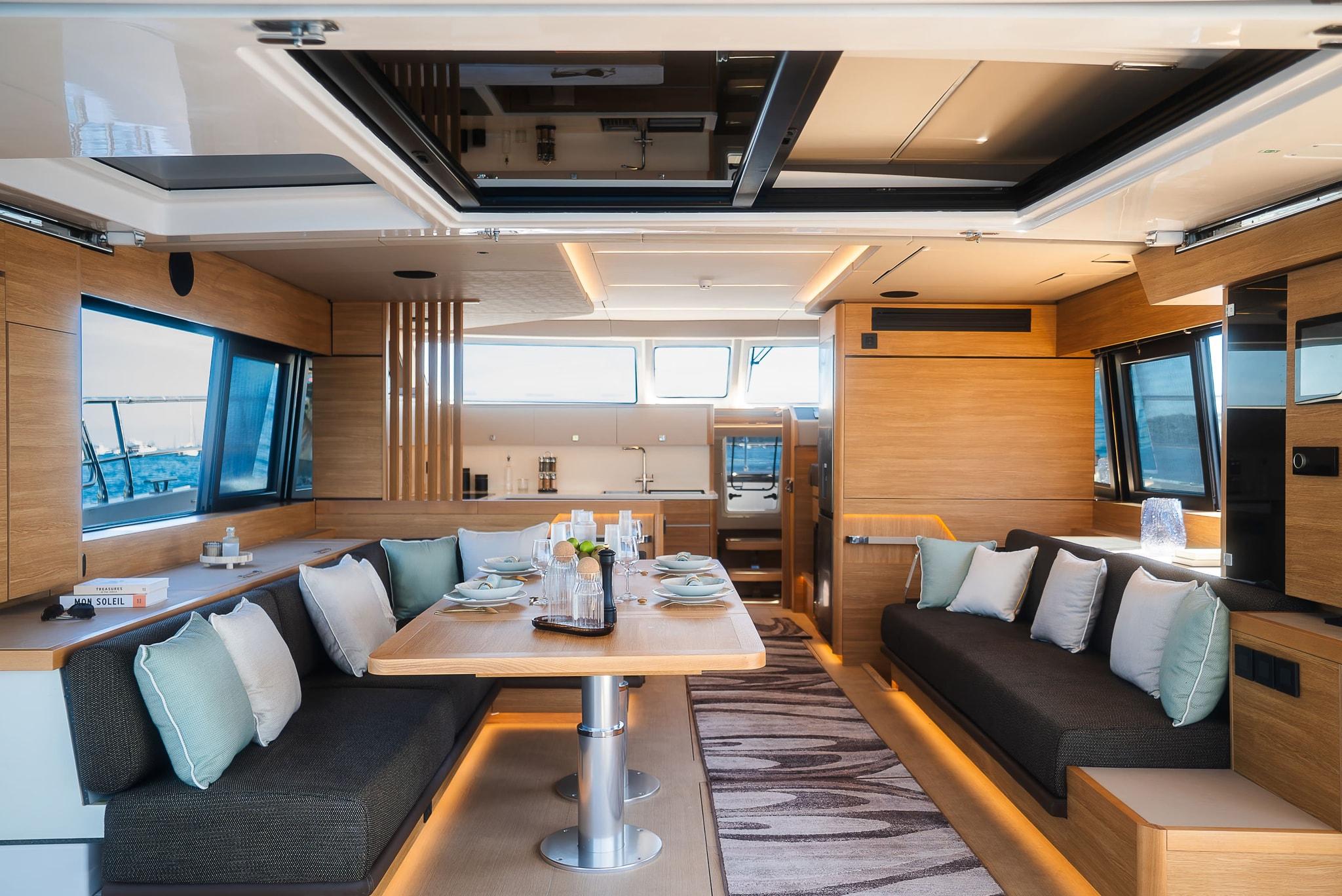 The saloon from aft, the table laid between settees under a long overhead window