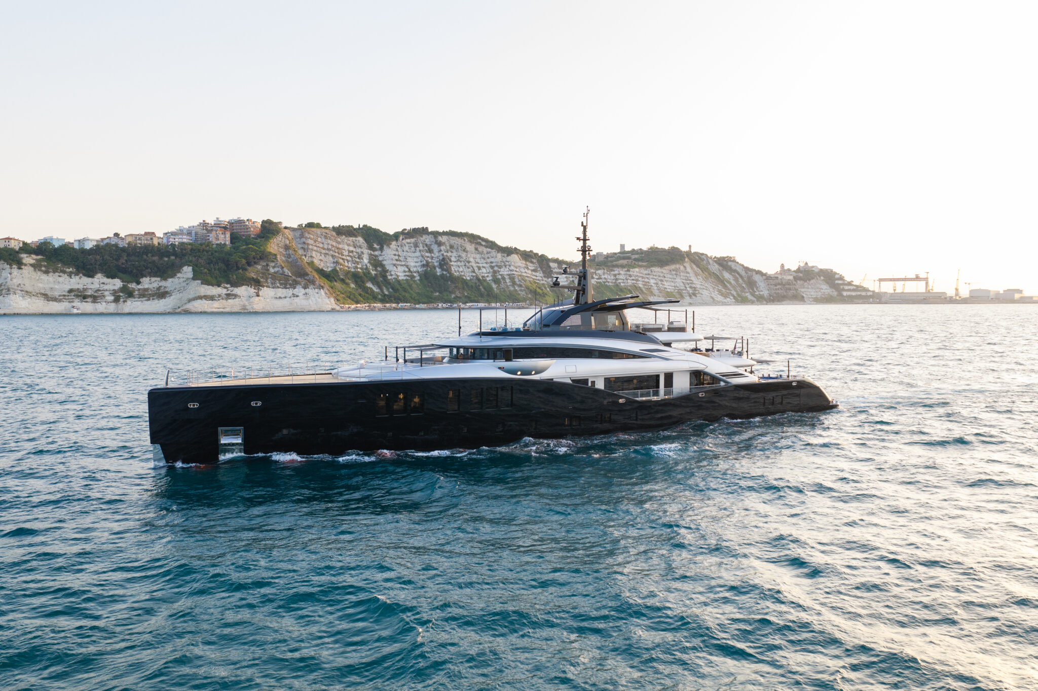 Sea Raider X seen in full profile from port, with the cliffs and shipyard cranes of Ancona behind her