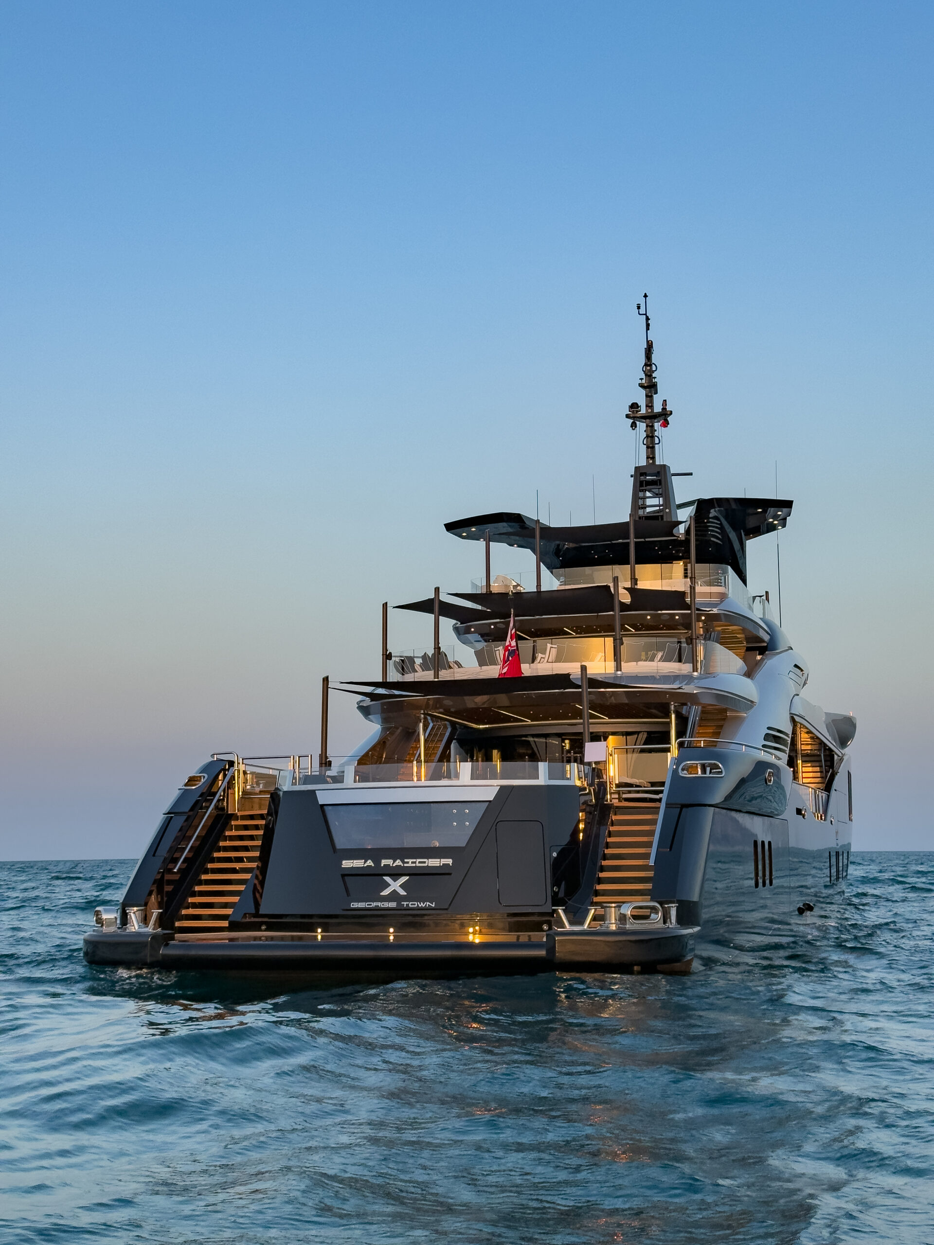 Sea Raider X from astern at dusk, her name and George Town home port on the transom, with twin teak staircases down to the bathing platform