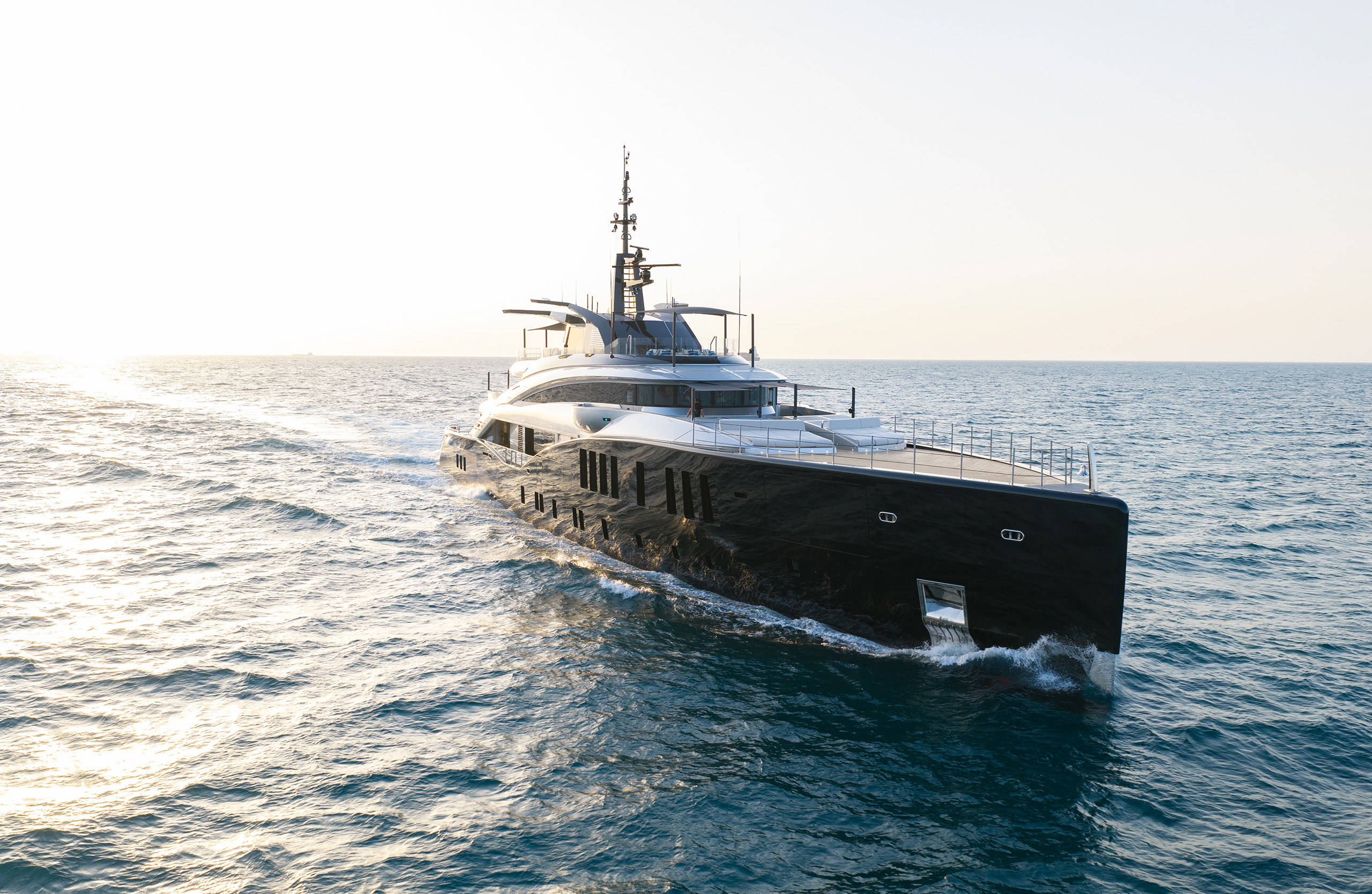 A photograph of Sea Raider X running towards the camera into low sun, a black steel hull with a silver superstructure above