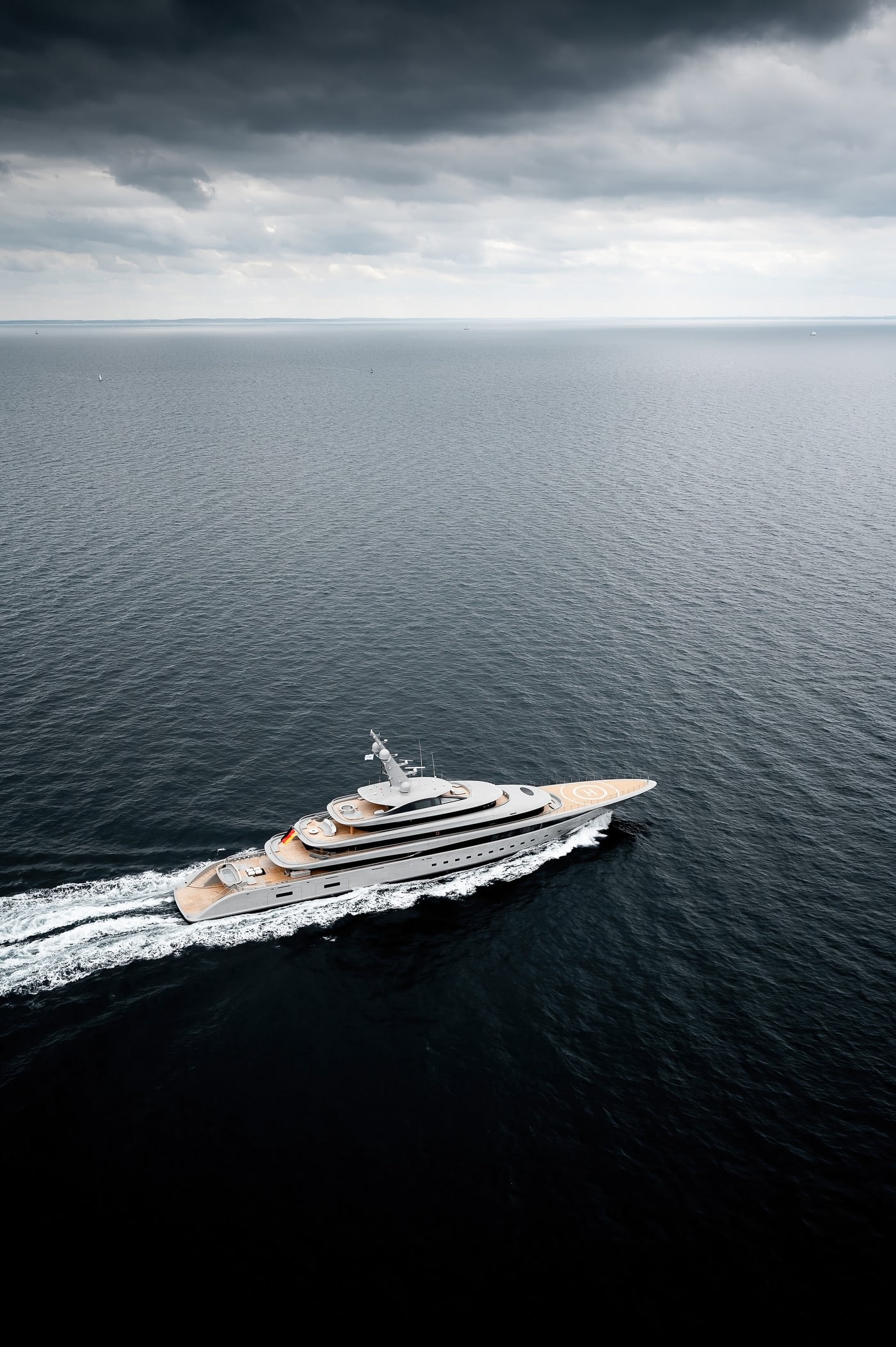 A tall aerial photograph of Nixie under way on a grey sea under heavy cloud, her helipad marked on the foredeck