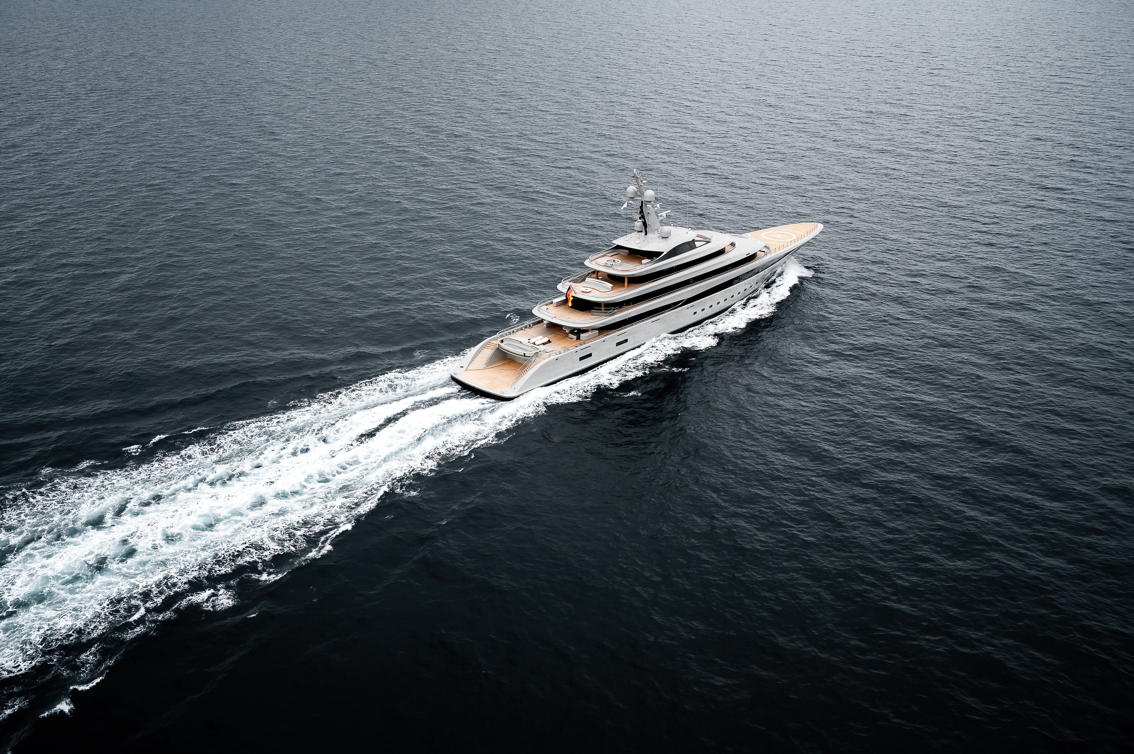 A wide aerial photograph of Nixie running across open water, a long silver hull with teak decks and four levels of superstructure aft