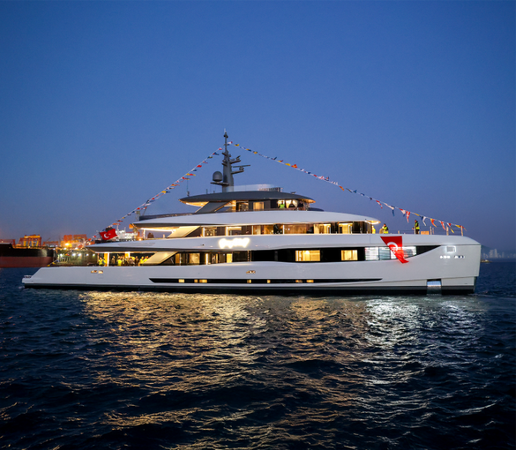 Gray Wolf's four decks seen from the water at dusk, her interiors lit through full-height glazing
