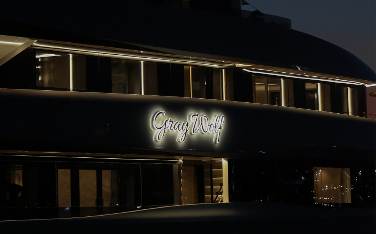 The illuminated Gray Wolf nameplate in script on the yacht's side at night