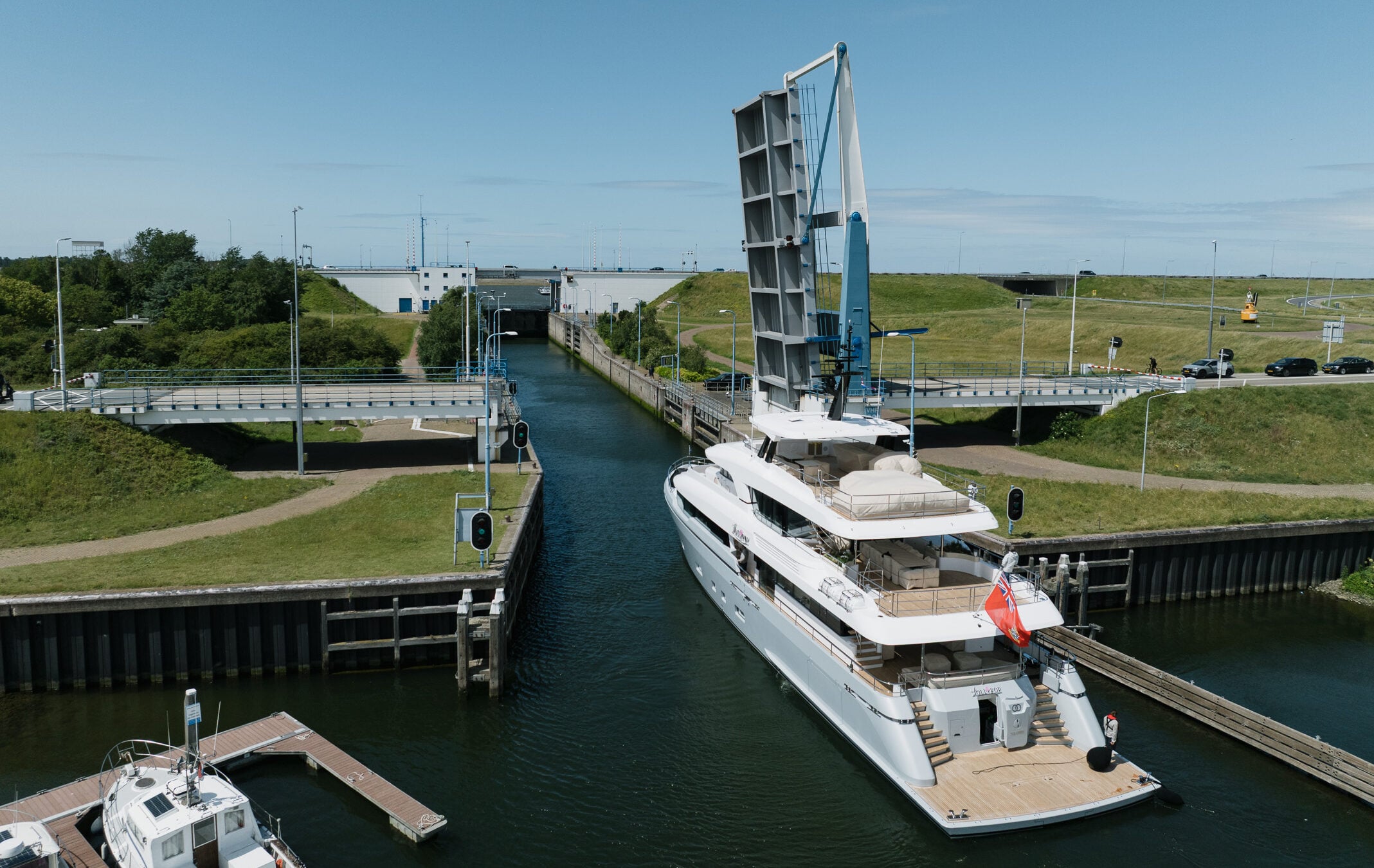 LOLLIPOP in a Dutch canal lock with the bascule bridge raised ahead of her, seen from above and astern, a crew member on the foredeck and grass banks either side