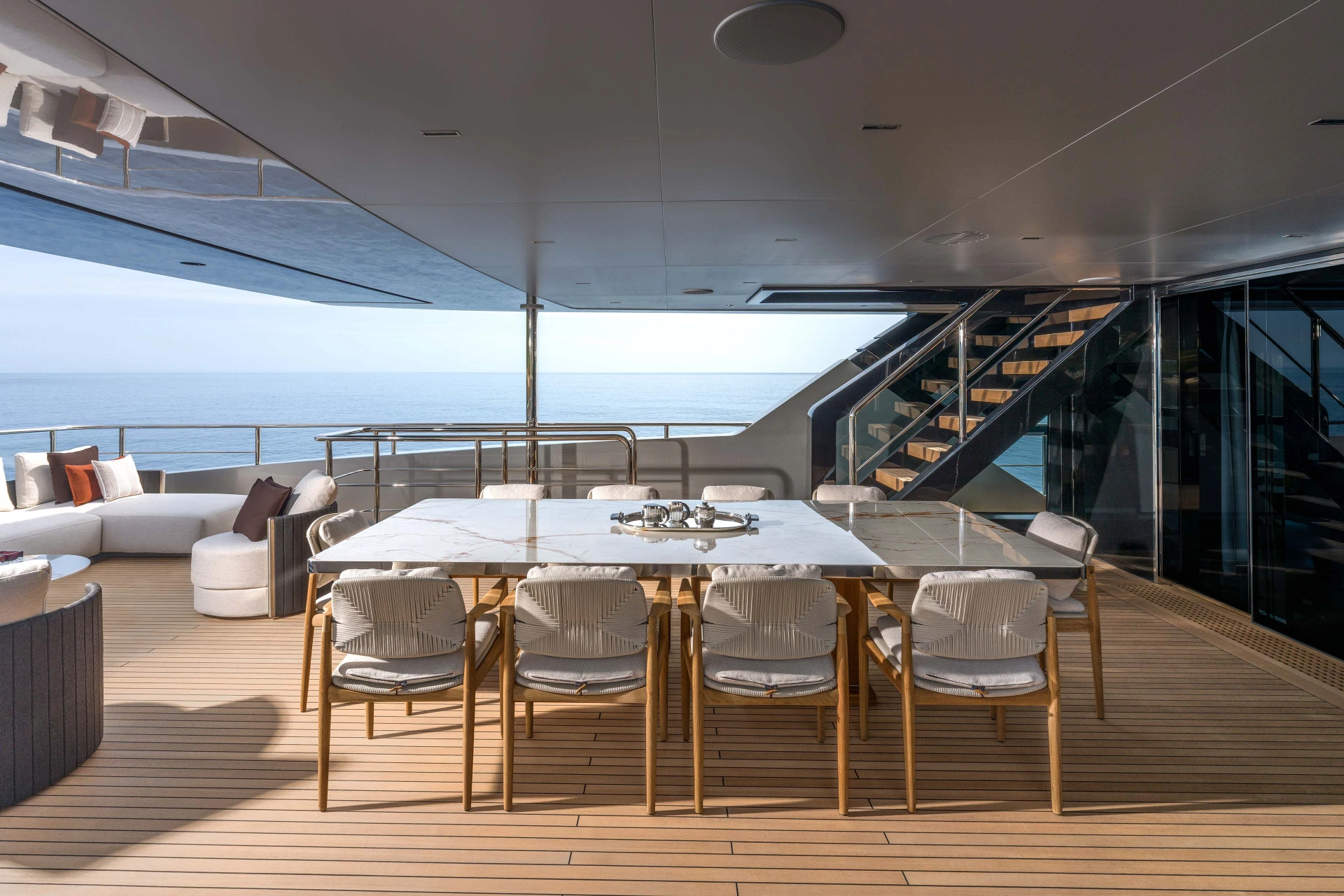 A photograph of the aft deck dining area, a marble table for ten under the deck above with a teak stair climbing to starboard