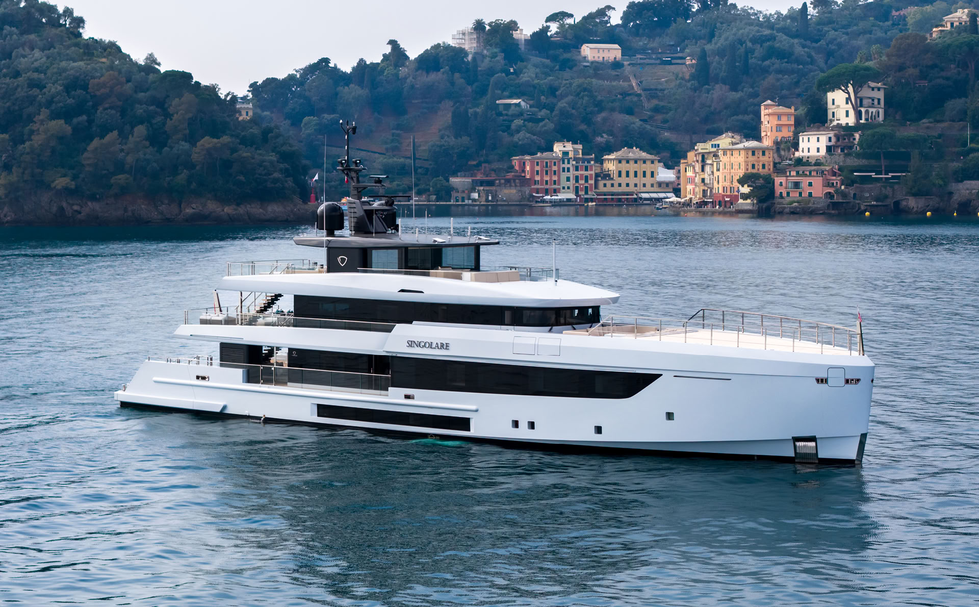 A photograph of Singolare at anchor off Portofino, her white hull and three decks against the coloured houses of the harbour